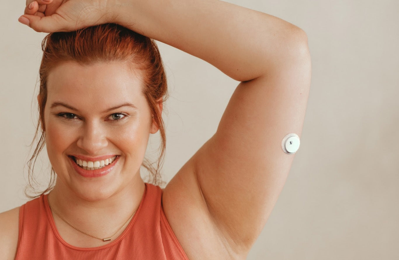 A smiling woman wearing a continuous glucose monitor on her upper arm